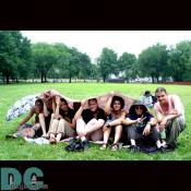 A group sits on the grass, attempting to stay dry and waiting for the concert to begin.