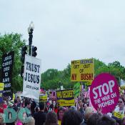 Marchers on Constitution Avenue.  One marcher holds a message for the President - HEY -- GEORGE GET OUT OF MY BUSH while another holds a pink sign reading STOP THE WAR ON WOMEN.