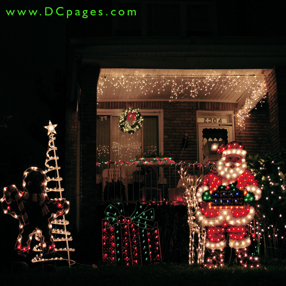 A lit ginger bread man holding a candy cane, Santa Claus, a reindeer, a green and red present, wreath, and lights fill this yard with good cheer.