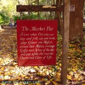 Sign for 'The Market Fair' reads: "A time when Citizens can buy and sell, eat and drink, play Games and Music, attend their Militia, exchange Gossif and News of the day and put aside the routine Chores and Cares of Life.