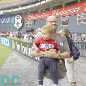 A smiling father was holding his cute son wearing a "SOCCER" shirt. 