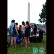A group of friends pick a good location in front of the Washington Monument to view the fireworks display after dusk.