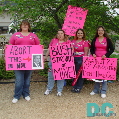 Four Pro-Choice activists hold demonstration signs - ABORT THIS -> [Picture of President George Bush] IN NOV. - BUSH, STAY OUT, OF, MINE - FREEDOM [check box] MY BODY, [check box] MY CHOICE, [check box] NO WAR, [check box] NO BUSH, GET SOME - AGAINST ??, ?? ABORTION, DONT HAVE ONE -