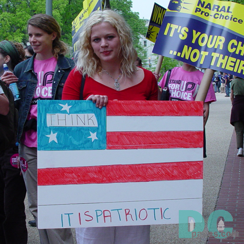 A marcher holds a representation of the US flag that asks the reader to THINK because IT IS PATRIOTIC.