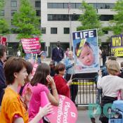 A Pro-Life advocate holds a picture of a baby with the statement LIFE while Pro-Choice marchers pass by.