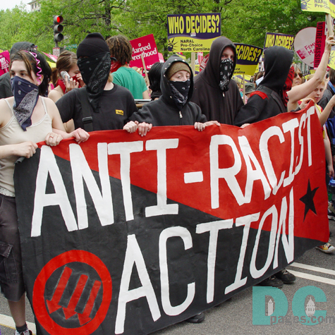 A group of marchers wearing black carry an ANTI-RACIST ACTION banner.