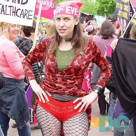 Pro-Choice advocate wears an AXIS OR EVIL t-shirt, WEAPON OF MASS SEDUCTION shorts and a headpiece that reads OF EVE.