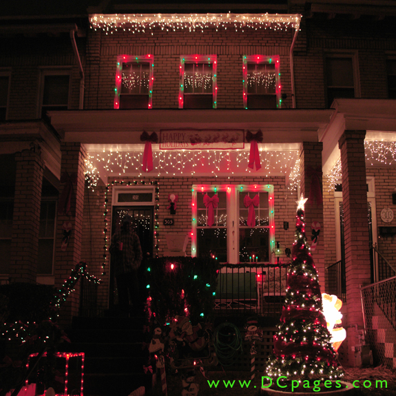 "A Happy Holiday's" sign with red ribbons on each side showcases a house filled with many outdoor decorations.