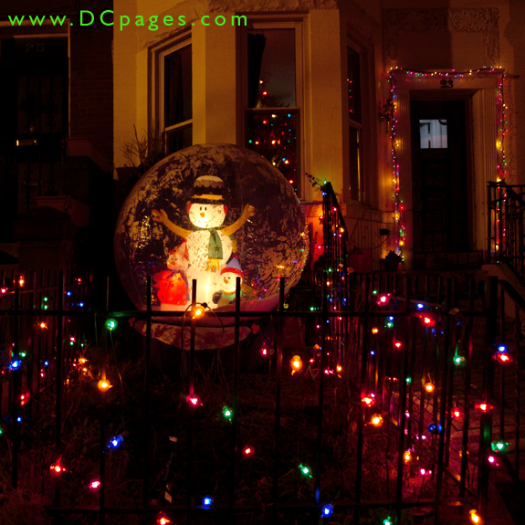 A giant inflatable snowman and snow children are surrounded by a dazzling display of lights. A Christmas tree can be seen in the window.