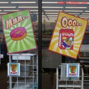 Display signs for Sprinklicious pink donuts and KrustyOs breakfast cereal on available at the Bladensburg, MD Kwik-E-Mart.