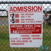 Sign - ADMISSION - $7.00 PER PERSON AGE 7-59 - $5.00 PER PERSON AGE 3-6 and 60 and OVER - MIDWAY OPEN 3 PM - WEATHER PERMITTING - NO RAINCHECKS OR PASSOUTS - PARKING, GRANDSTAND and MIDWAY SHOWS ARE INCLUDED IN ADMISSION.
