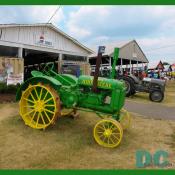 A antique JOHN DEERE tractor is parked in front of the PRINCE WILLIAM ANTIQUE TRACTOR CLUB exhibit barn.