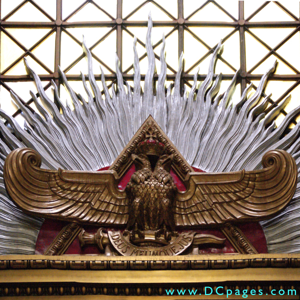 Bronze sculpted double-headed eagle spreads its wings in front of a red pyrimid.