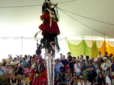 The Dogon dancer on stilts dwarfs over the fellow Dogon dancer, the crowd looks on in awe