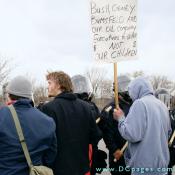 Demonstrators stand their ground in front of the riot police. One demonstrator holds up a sign - Bush, Cheney, Runsfeld and our oil company Executives to WAR - $ Not $ Our Children.
