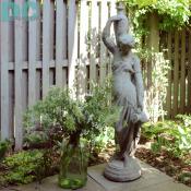 Sculpture of woman carrying a pot is next to fresh cut flowers.