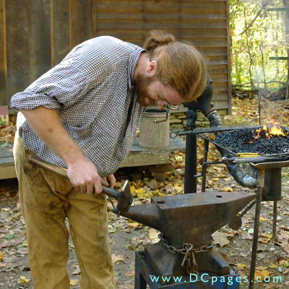 Blacksmith Eric Zieg hammers a metal rod over a large iron anvil. The coal burning stove in the background is used to heat up the metal.