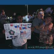 A child displays a poster he made for the 'Freedom Walk.' There is a drawing of the World Trade Center, The Pentagon, and the United States Flag. The Poster is captioned - WE WILL ALWAYS REMEMBER YOU.