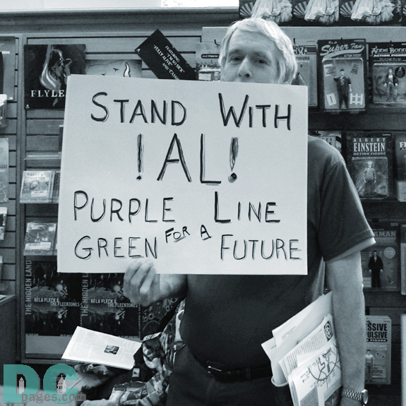 An metro transportation activist holds up a sign that states 'STAND WITH AL!, PURPLE LINE, GREEN FOR A FUTURE.' 