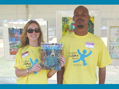 ICAF staff Amanda Kah and Chris Miles hold the festival issue of the ChildArt Magazine in front of the Child Finalist Art display